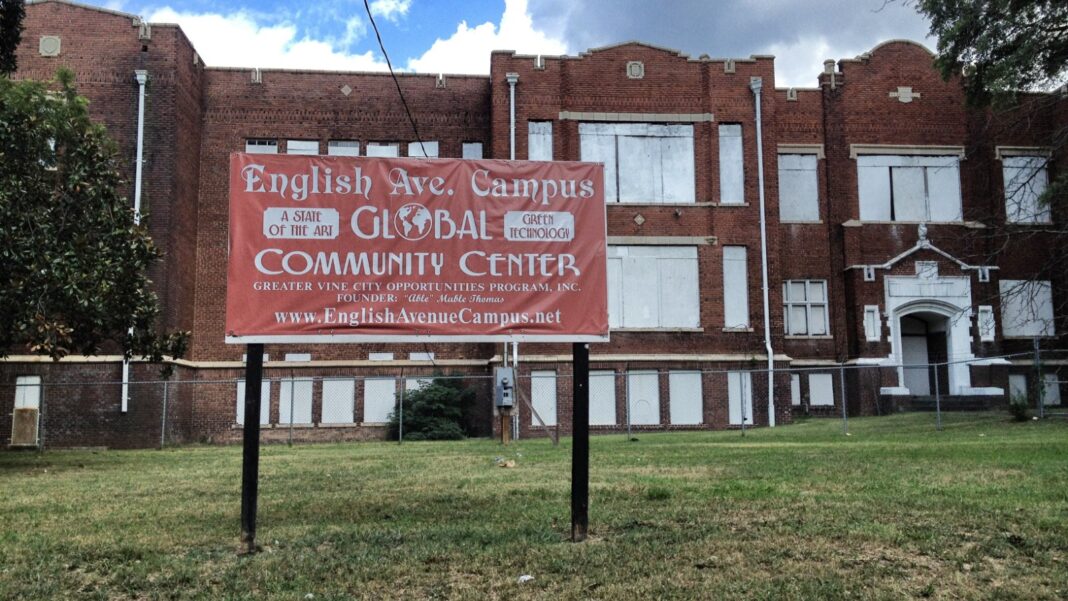 A three-story brick former school building with a community-center sign on the lawn in front