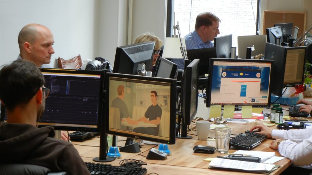 AI Coding Tools Increase Commits Much More Than Finished Software, Study Finds Software developers work at desks with multiple computer monitors in an office