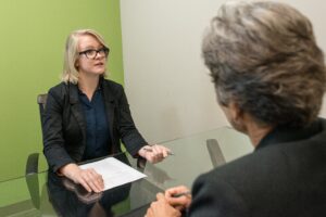 A job candidate holding a resume sits across a table from an interviewer