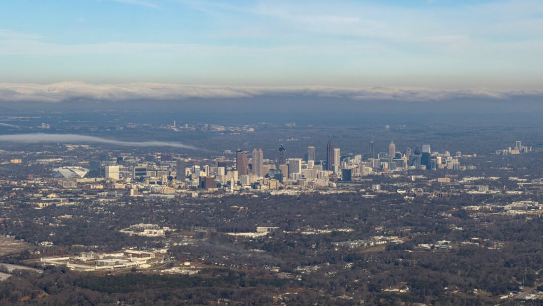 Aerial photograph of the Atlanta metro area stretching to the horizon, with the downtown skyline rising in the middle distance