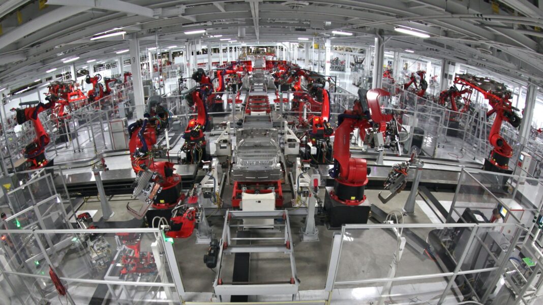 August Durable-Goods Orders Hold Nearly Flat as Transportation Softens Rows of red industrial robot arms working on car bodies along a factory assembly line