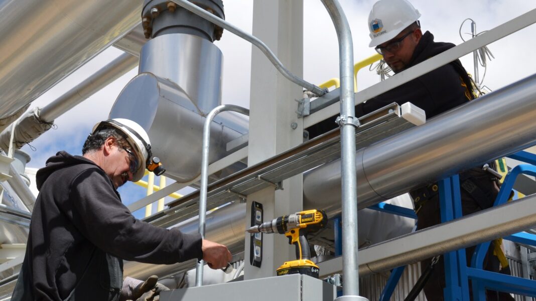 Data-Center Construction Spending Jumps 57% as Nonresidential Trade Contractors Add 86,000 Jobs Two electricians in hard hats install conduit and a mounting bracket on a steel pipe rack at a construction site