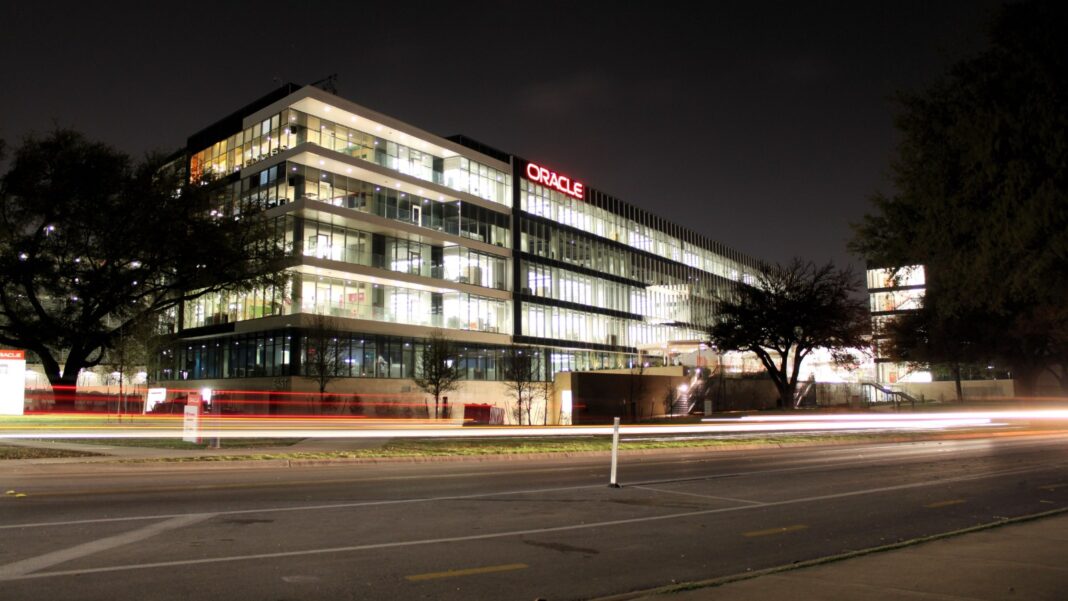 Leaked Oracle Cloud Layoff Records Detail Which U.S. Teams Were Affected Oracle's multi-story glass office building in Austin lit up at night, with light trails from passing traffic