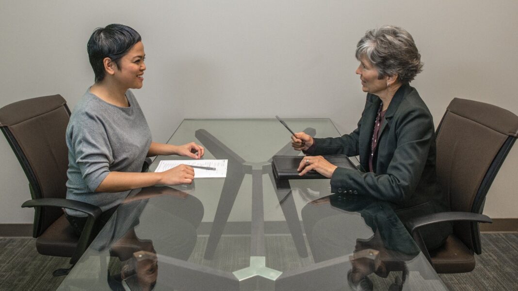 LinkedIn’s Hiring Assistant 2 Puts Applicant Trust and Recruiter Workflow at the Center Two women sit across a glass table from each other during a job interview, one taking notes