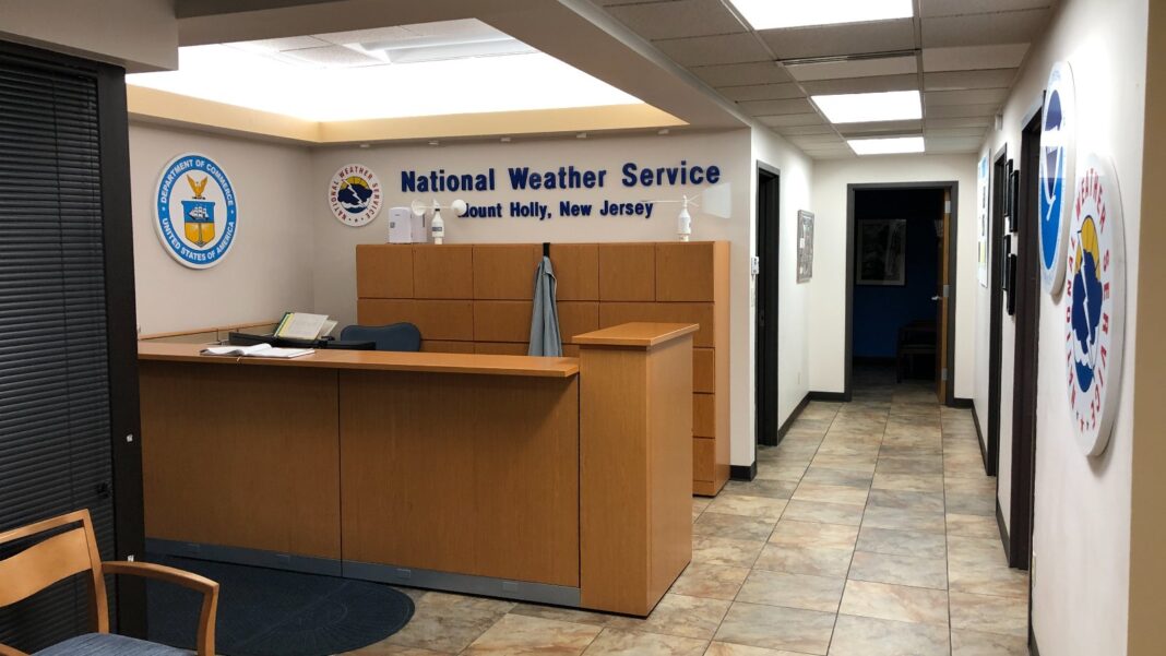 An unstaffed wooden reception desk in an office lobby with agency seals on the wall and a hallway behind it