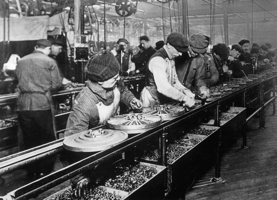 Productivity Gains Do Not Automatically Mean Headcount Cuts Workers stand along a moving assembly line at a Ford Motor Company plant in 1913