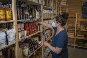 An employee in a mask stocks shelves of jarred and packaged goods in a small farm store