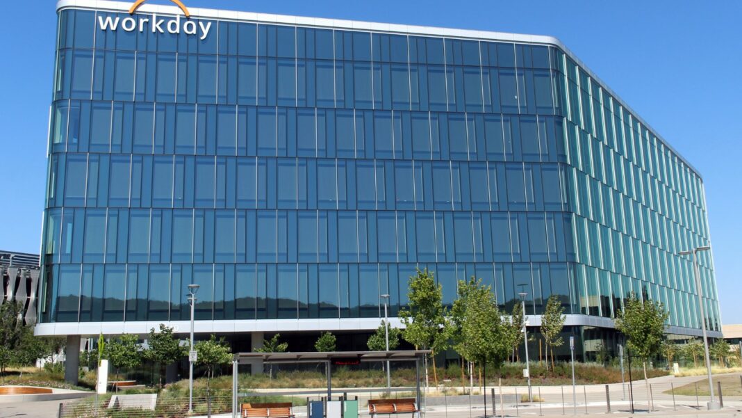 A modern glass office building with the Workday logo on its top corner under a clear blue sky