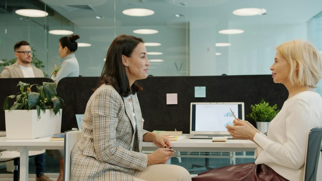 HubSpot to Cut Nearly 660 Jobs as It Flattens Its Organization Coworkers discussing work at a laptop, used as a representative workplace image.