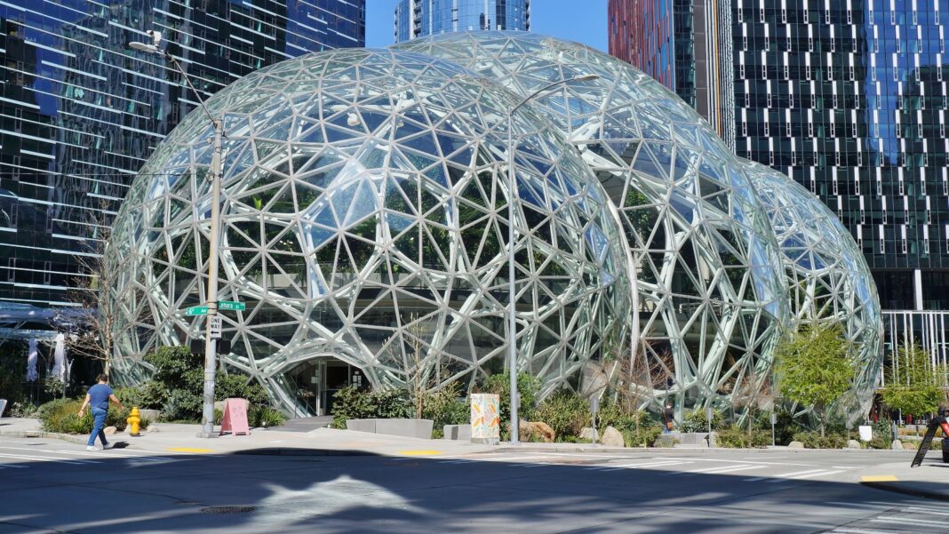 Amazon Makes Another Round of Corporate Job Cuts, Concentrated in Its Stores Business Three large glass-and-steel domes in front of office towers on a city street
