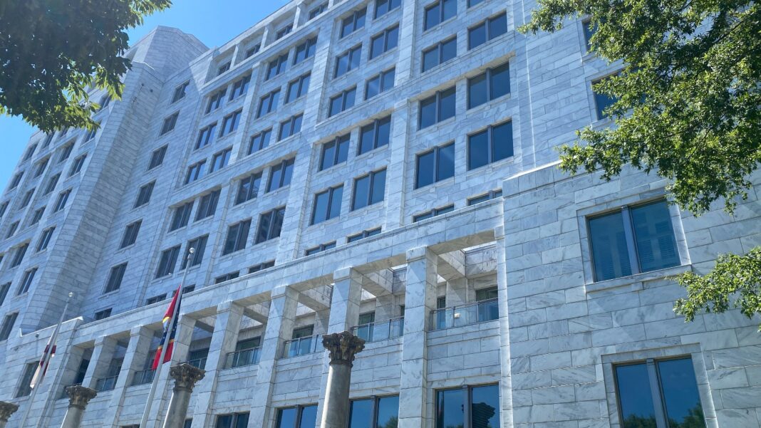 Atlanta Fed: Job Gains Have Spread Beyond Health Care, but the Labor Market Is in a Holding Pattern Low-angle view of a multistory white stone office building with rows of windows, columns at its base and trees in the foreground under a blue sky.