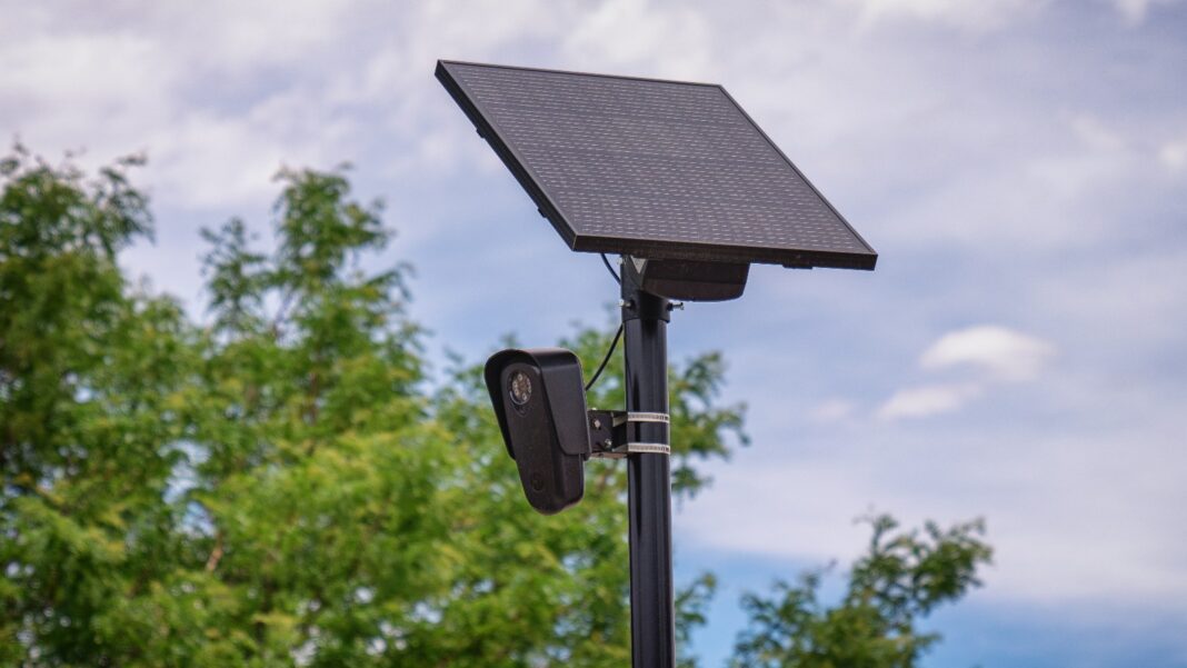 Atlanta-Based Flock Safety Reportedly Plans to Cut About 270 Jobs, 18% of Its Staff A black camera and a solar panel mounted on a metal pole against a partly cloudy sky, with trees behind