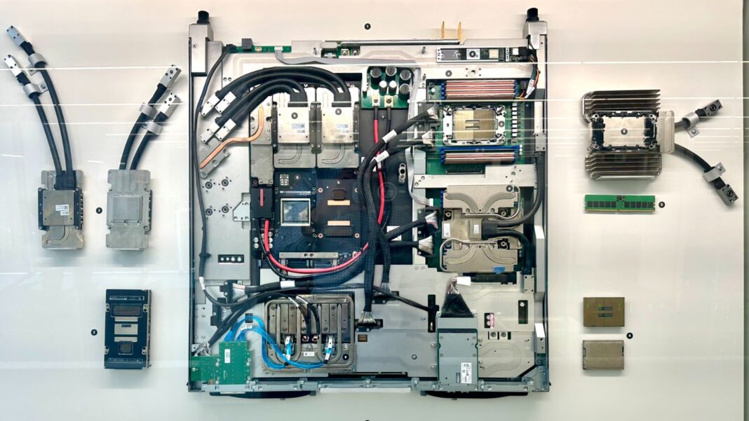 A disassembled computer server blade laid out on a white panel, with processors, cooling blocks, coolant hoses and connectors arranged around it