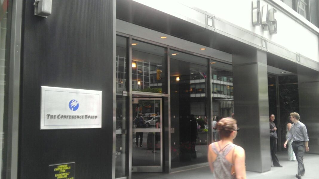 Conference Board CEO Confidence Falls to 46 in Q4 as More Executives Plan Workforce Cuts Glass office-building entrance with a silver plaque reading The Conference Board and pedestrians walking along the sidewalk