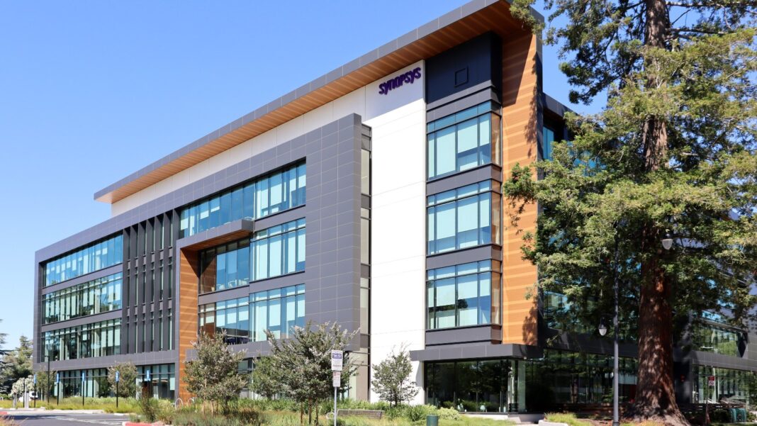 A modern four-story office building with glass, gray panels and wood trim beside a tall redwood tree