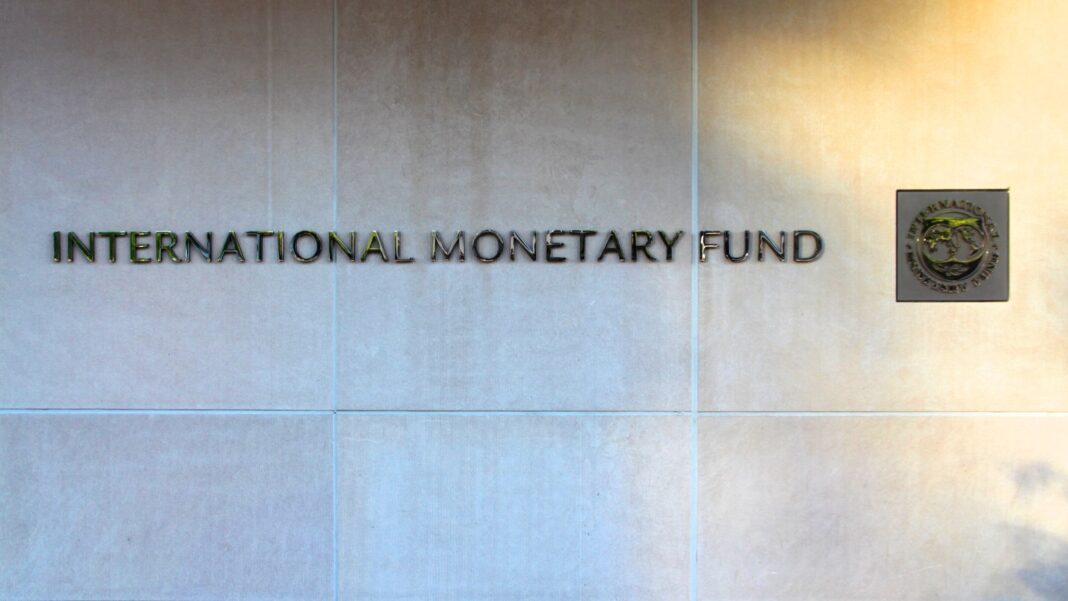 IMF Holds 2026 Global Growth Forecast at 3.1% and Says AI’s Effect on Jobs and Wages Is Still Limited Metal letters reading International Monetary Fund and a square seal mounted on a pale stone wall