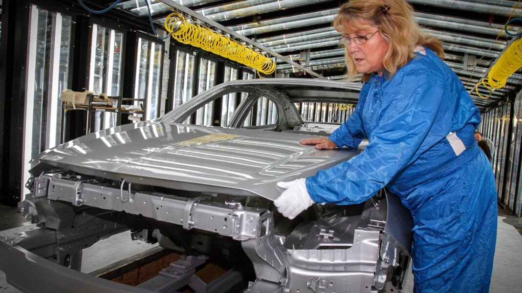 Factory Employment Gauge Strengthens as Eight Manufacturing Industries Report Growth A worker in a blue protective suit and gloves inspects an unpainted silver car body on an automotive assembly line