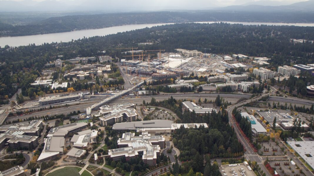 Aerial view of a large suburban office campus with construction cranes, highways and a lake under cloudy skies