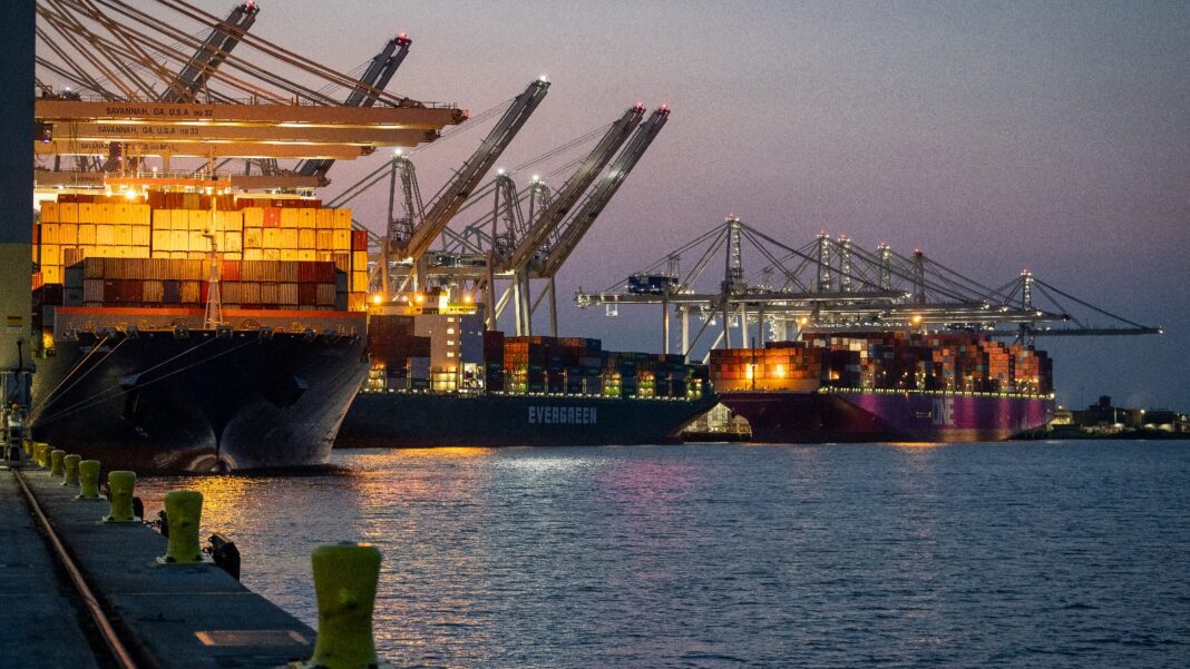 Army Corps Permit Clears Way for Savannah’s $2.3 Billion Third Container Terminal; Construction Set for 2028 Container ships stacked with containers sit under large ship-to-shore cranes at a port berth at dusk, with bollards along the quay in the foreground.