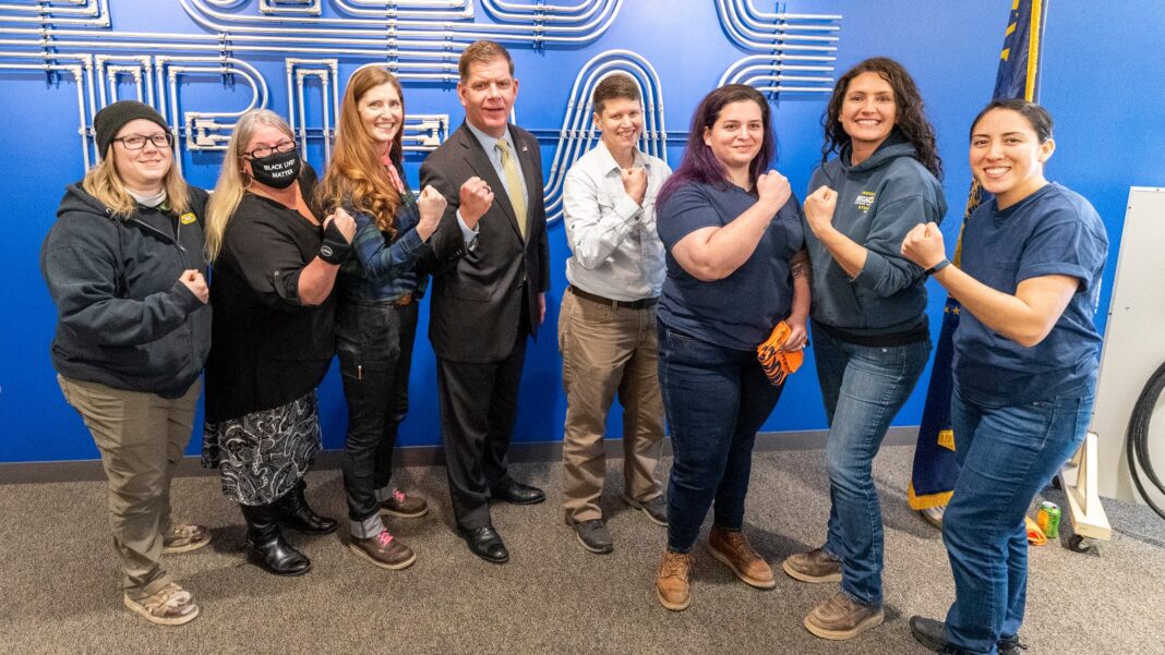 Skilled-Trades Report Projects 1.7 Million Annual Openings Through 2035; Georgia Is Among Gap States A group of women in work clothes raise their fists in front of a blue wall at an electrical training center, with a man in a suit in the middle