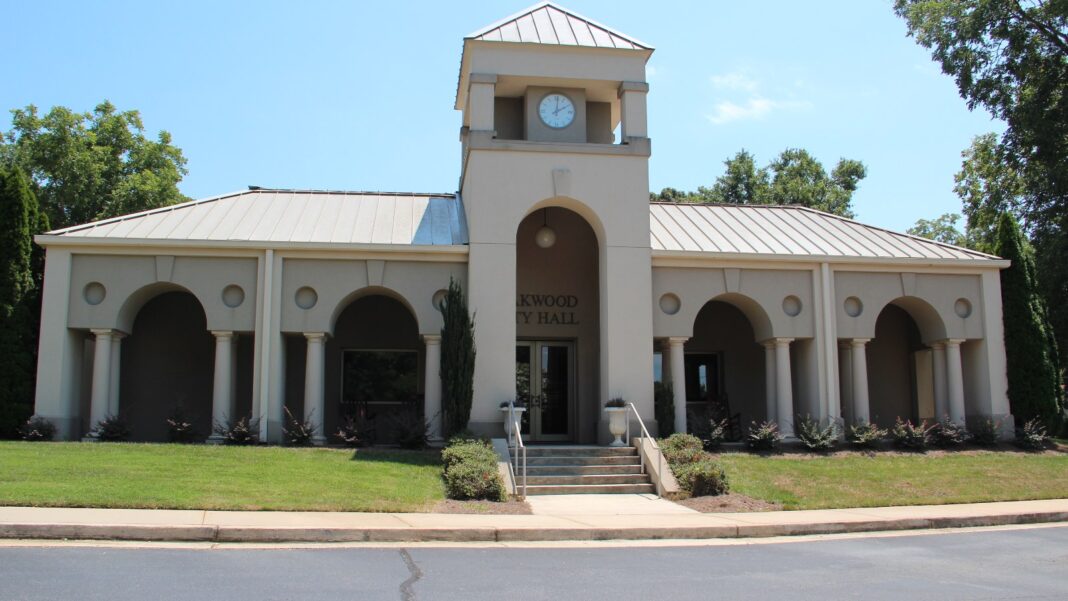 VDL Plans $77 Million Oakwood Expansion and About 120 Jobs in Hall County A single-story beige civic building with arched colonnades and a central clock tower, set behind a green lawn and shrubs under a blue sky.