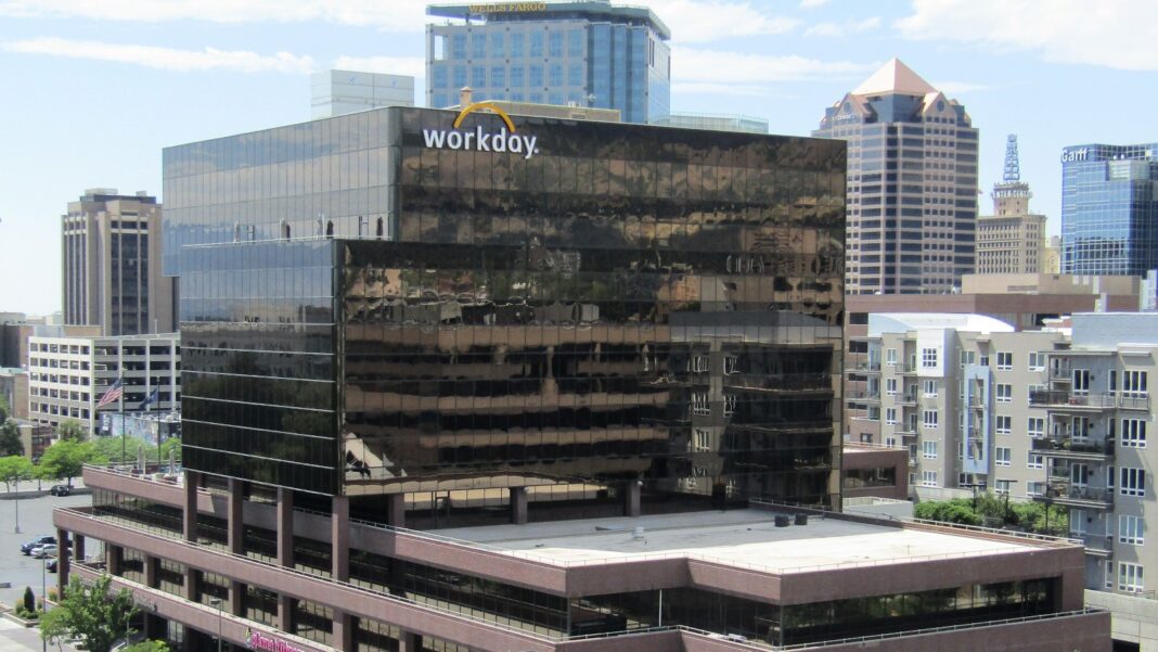 A dark glass office tower with a Workday sign at the top, rising from a lower brown building among downtown high-rises